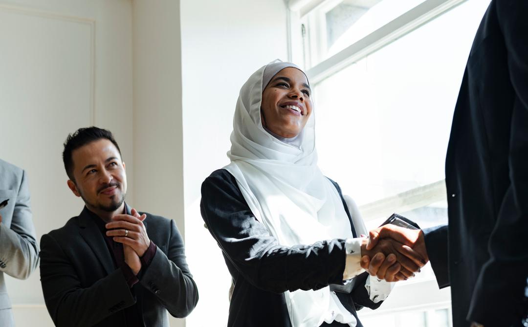 Several employees are praising a female employee, while the boss shakes her hand.