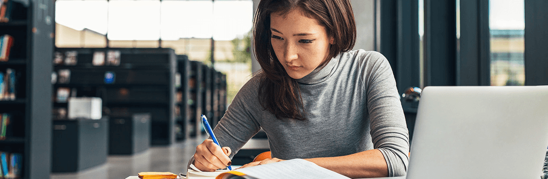 woman writing on book behind a table