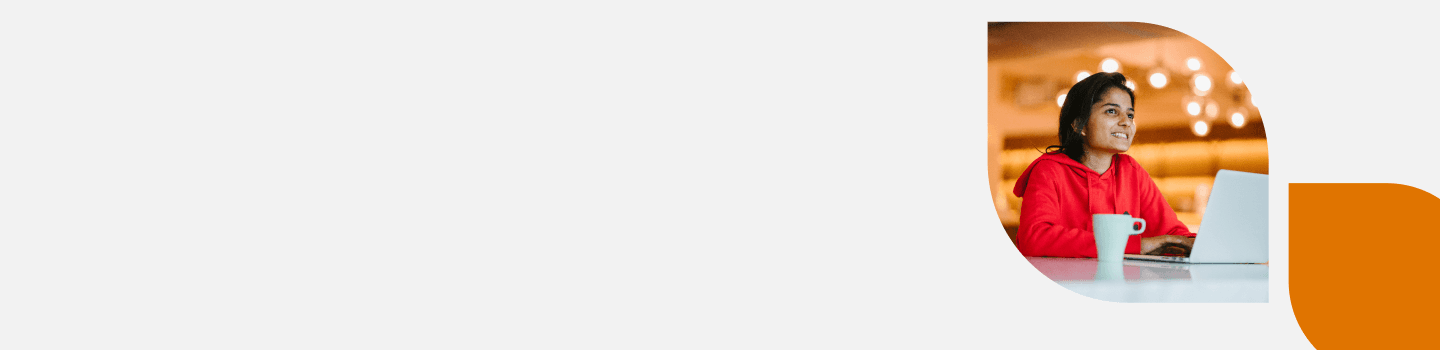 A person in a red hoodie sits at a desk with an open laptop and a white mug, smiling and looking to the side. The background has warm, blurry lights. The image is framed by an abstract orange shape on a plain backdrop.