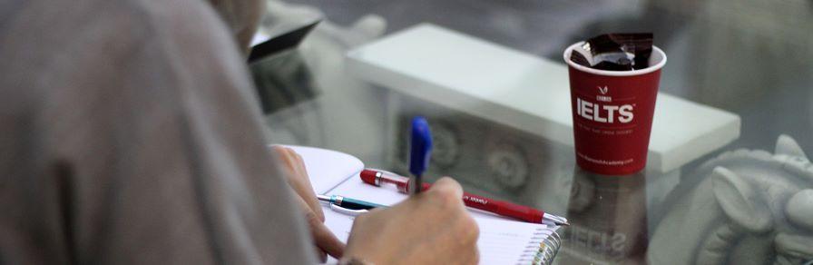 Writing on notepad with IELTS cup on the table