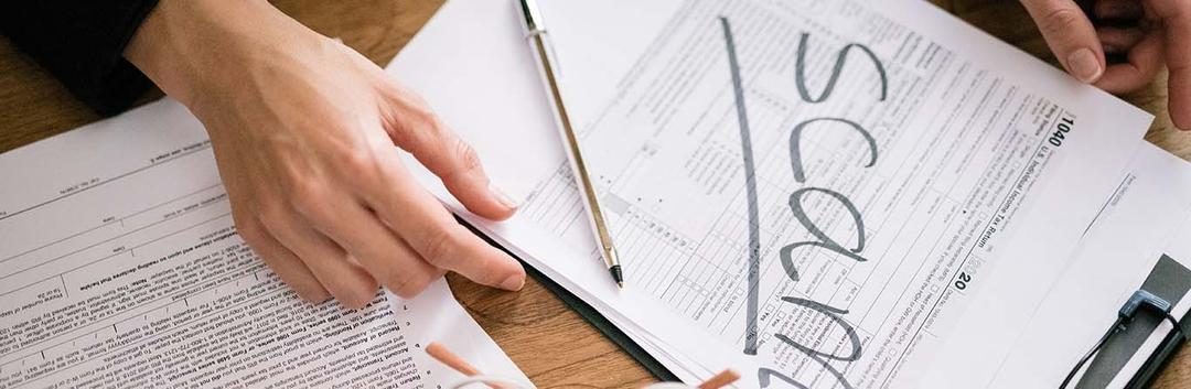 hand on table over paper saying 'scam'