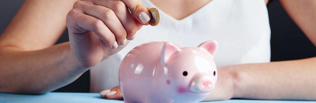 Hand inserting a coin into a pink ceramic piggy bank, symbolizing saving money and financial planning