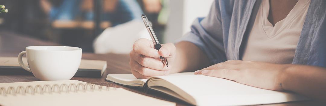 An international student writing in a notebook with a pen.
