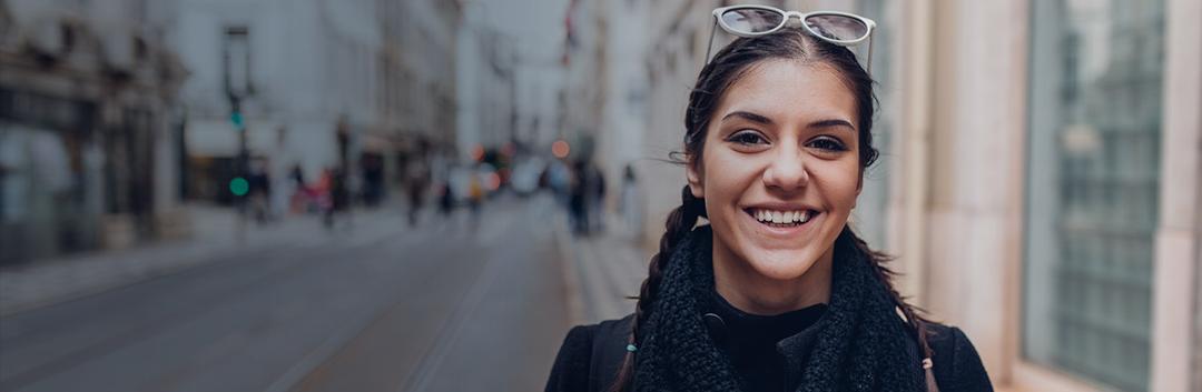 An international student wearing a scarf and sunglasses smiling